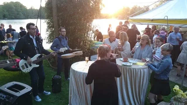 Sommerfest am See mit Live-Musik, festlicher Atmosphäre und fröhlichen Gästen bei Sonnenuntergang.