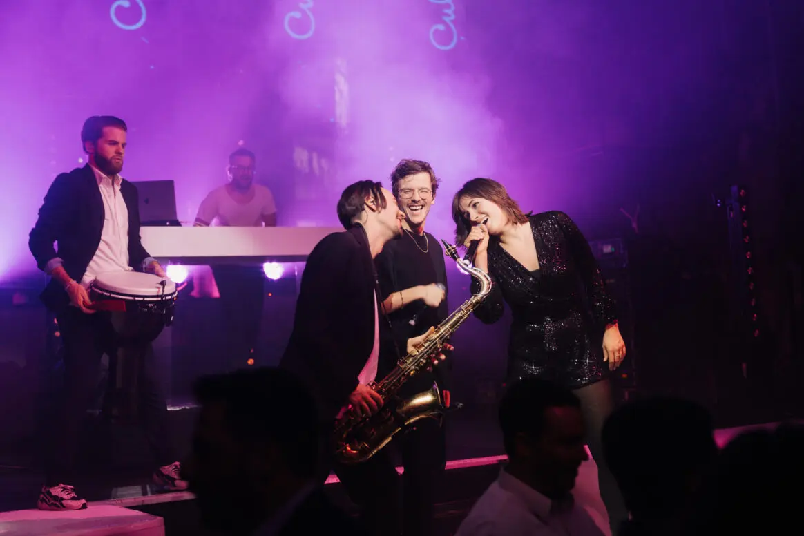 Live-Musik-Performance mit Sänger, Saxophonist, Drummer und begeistertem Publikum bei energischer Show.