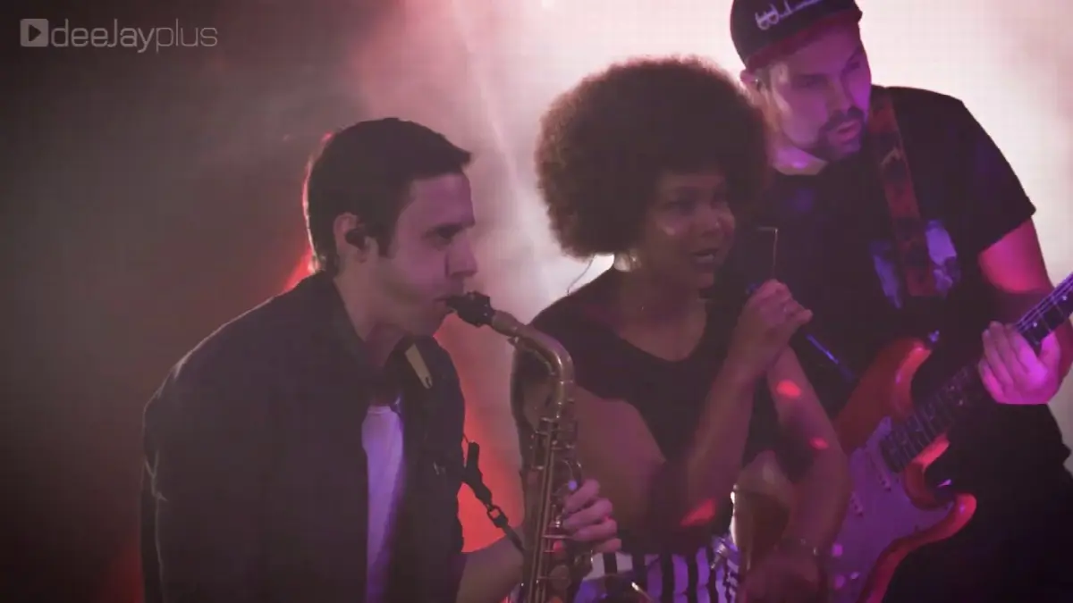 Live-Musikperformance mit Saxophon, Sängerin und Gitarrist bei energiegeladenem Konzert.