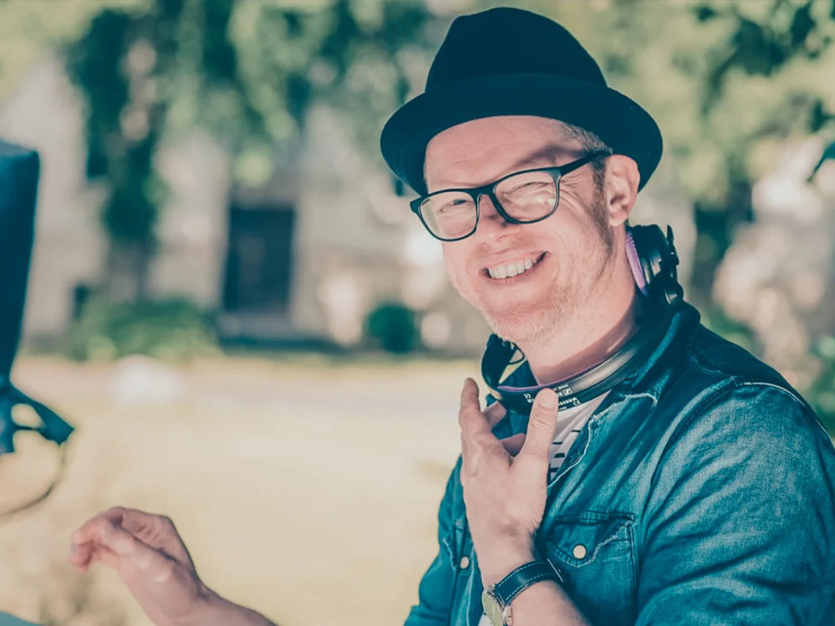 DJ Jocar im Freien mit Kopfhörern, lächelnd und in lockerer Kleidung bei Outdoor-Event.