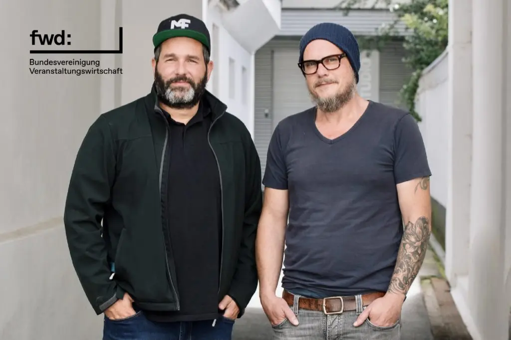 Zwei Männer in urbaner Umgebung, Musik und Veranstaltungsbranche, Verbindung zur Bundesvereinigung Veranstaltungswirtschaft.