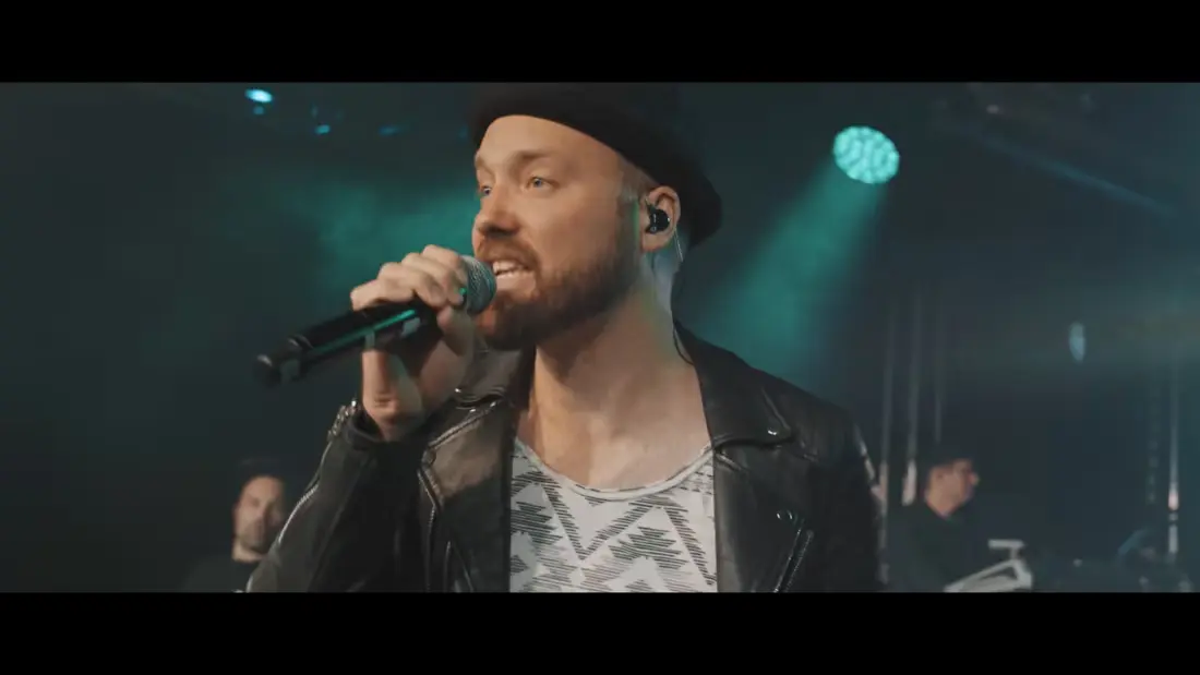 Musiker auf Bühne mit Lederjacke, Mikrofon und energiegeladener Live-Performance.