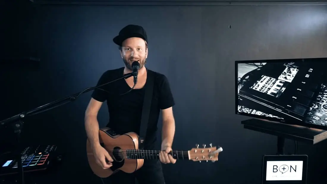 Musiker spielt akustische Gitarre in modernem Studio mit Technik und minimalistischem Design.