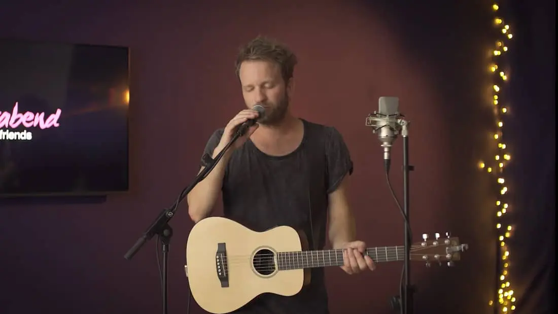 Musiker singt mit Akustikgitarre bei gemütlicher Live-Veranstaltung in entspannter Atmosphäre.