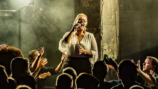 Live Musik Performance mit Sängerin, Publikum, Beleuchtung und intensiver Konzertatmosphäre in kleinem Venue.